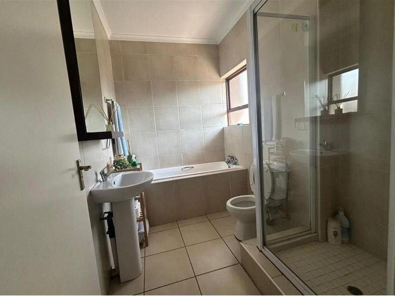 A functional bathroom featuring a pedestal basin, built-in bathtub, and a separate shower enclosure with neutral wall and floor tiling.