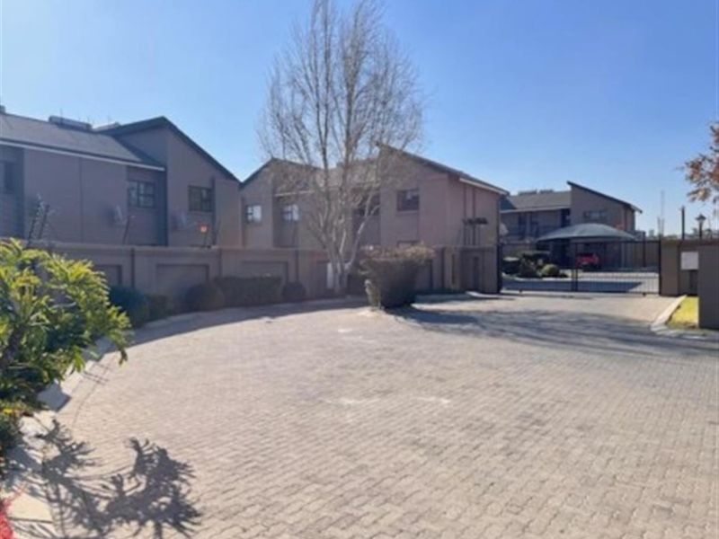 A view of the townhouse complex entrance featuring a paved driveway, perimeter walling, and secure gated access with carport parking.