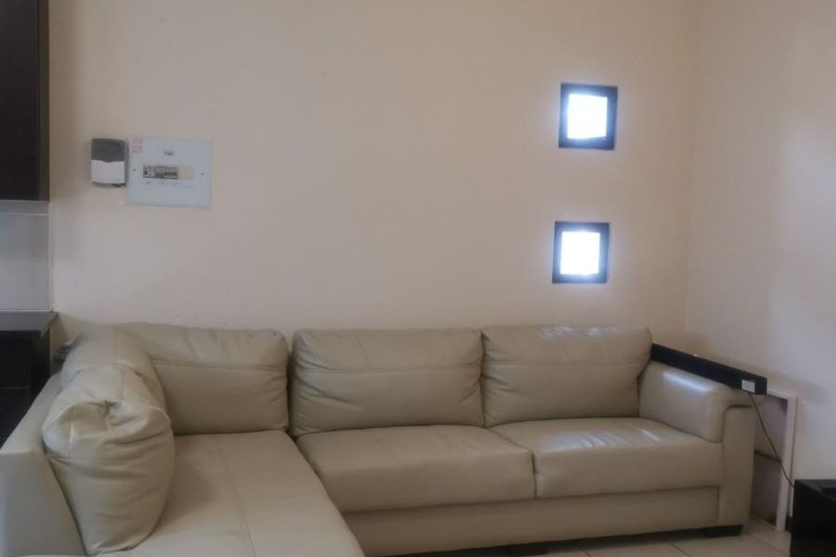 A living room area featuring tiled flooring, cove cornicing, and two small square windows, providing a functional and neutral space.