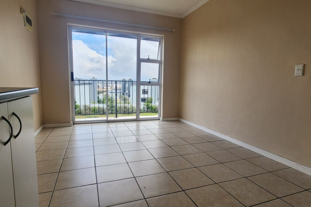 An empty living area featuring tiled flooring and a sliding glass door that opens onto a balcony with exterior views.