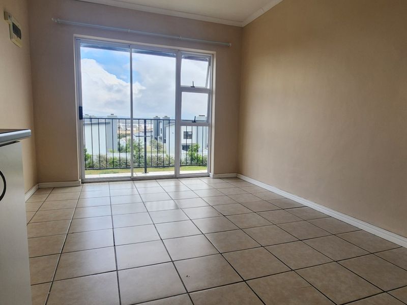 An empty living area featuring tiled flooring and a sliding glass door that opens onto a balcony with exterior views.