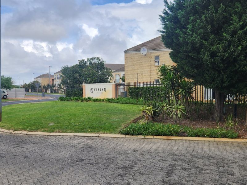 Street view of the Viking Villas complex entrance, featuring paved driveway access, well-maintained landscaping, and secure perimeter fencing.