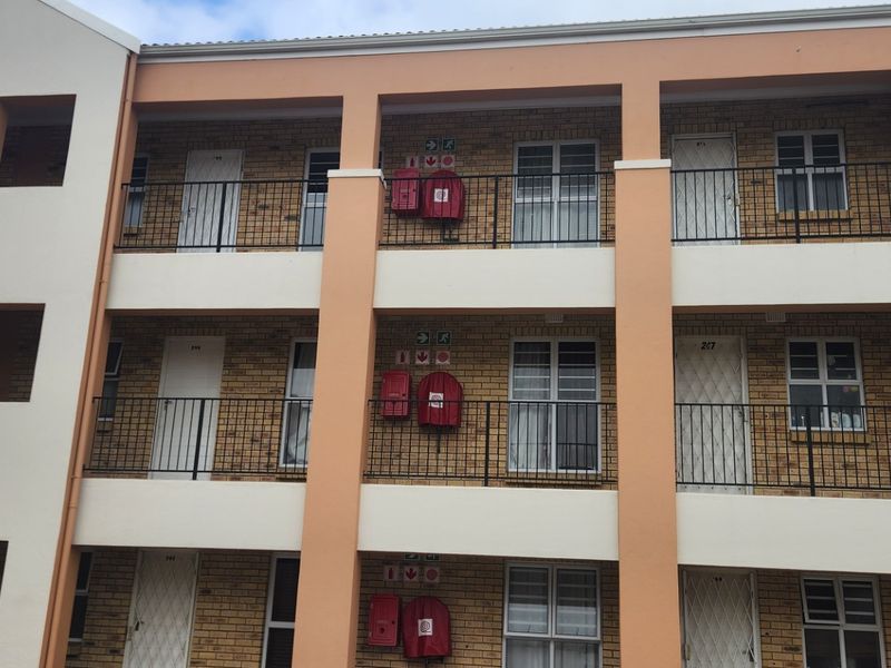 Exterior view of a multi-story apartment complex featuring brick facade, metal balustrades, and visible fire safety equipment on each level.