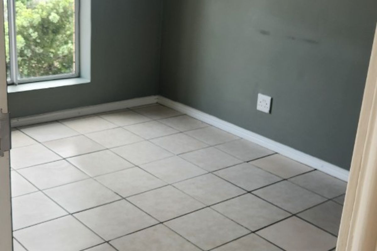 An empty bedroom featuring neutral tiled flooring, grey painted walls, and a window providing natural light.