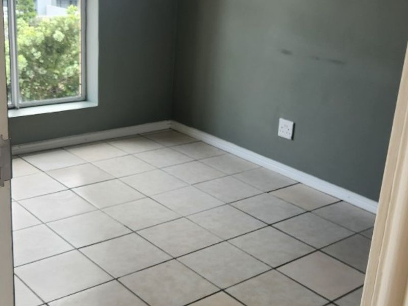 An empty bedroom featuring neutral tiled flooring, grey painted walls, and a window providing natural light.
