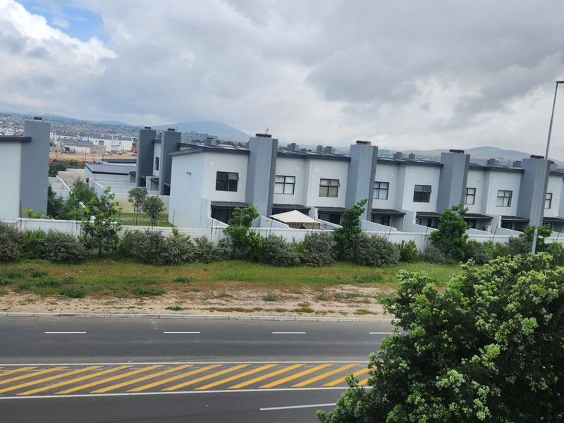 A view of the rear elevation of a modern apartment complex, featuring uniform architectural design, boundary walls, and proximity to a public road.