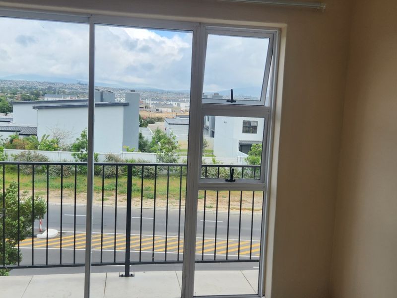 A clean, empty balcony featuring a metal balustrade and sliding glass door access, offering an elevated view of the surrounding neighborhood.