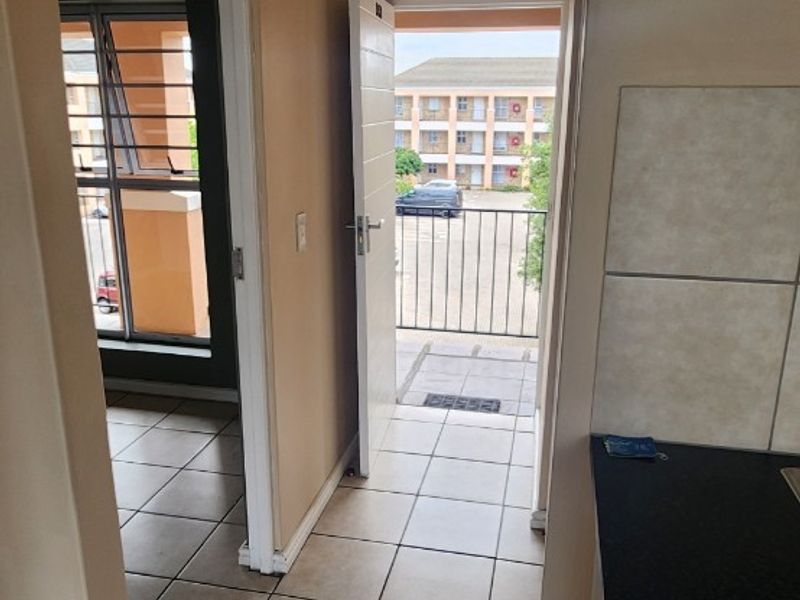 A tiled hallway providing access to a balcony and adjacent living space, featuring neutral wall tones and a functional kitchen counter area.