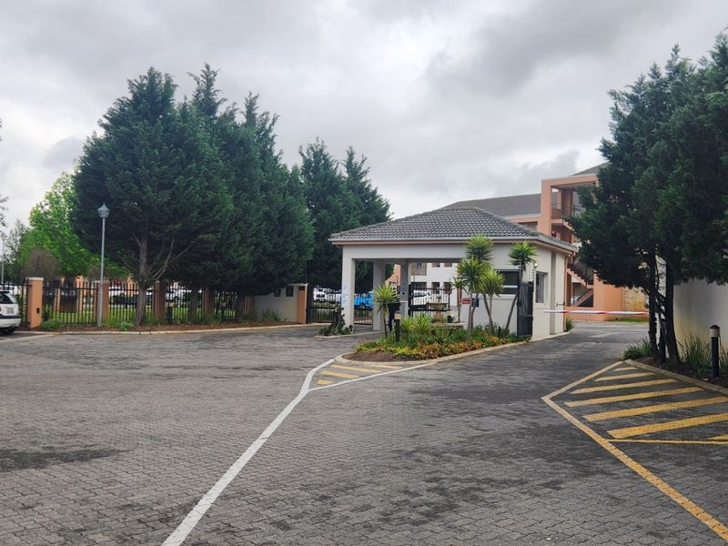 The entrance to the apartment complex features a secure gatehouse, paved driveway, and established perimeter landscaping.
