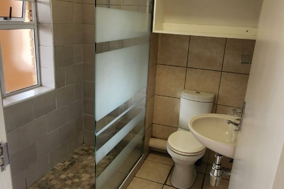 A functional bathroom featuring a walk-in shower with a frosted glass screen, pedestal basin, toilet, and wall-mounted storage shelving.