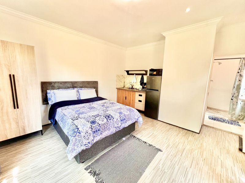 Open-plan studio cottage featuring a compact kitchenette with marble-look splashback, laminate flooring, and an en-suite bathroom with a shower.