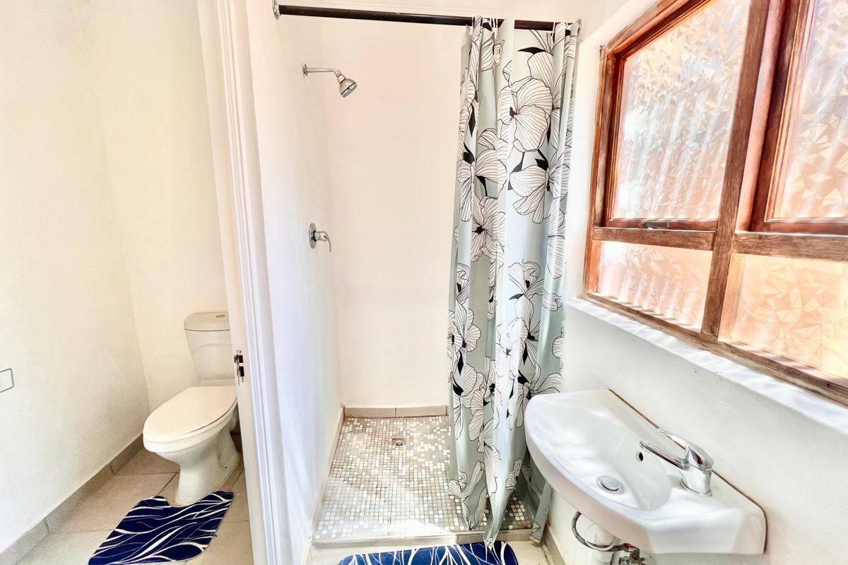 A functional bathroom featuring a shower with mosaic tiling, a wall-mounted basin, and a separate toilet area with natural light from a timber-framed window.
