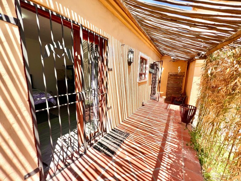 A covered patio area featuring terracotta tile flooring, a rustic wooden pergola, and a security gate providing access to the interior.