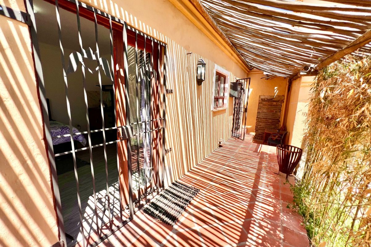 A covered patio area featuring terracotta tile flooring, a rustic wooden pergola, and a security gate providing access to the interior.
