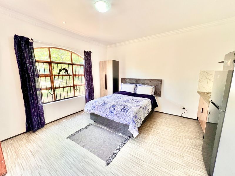 A well-lit bedroom featuring laminate flooring, an arched window with security bars, and built-in cabinetry.