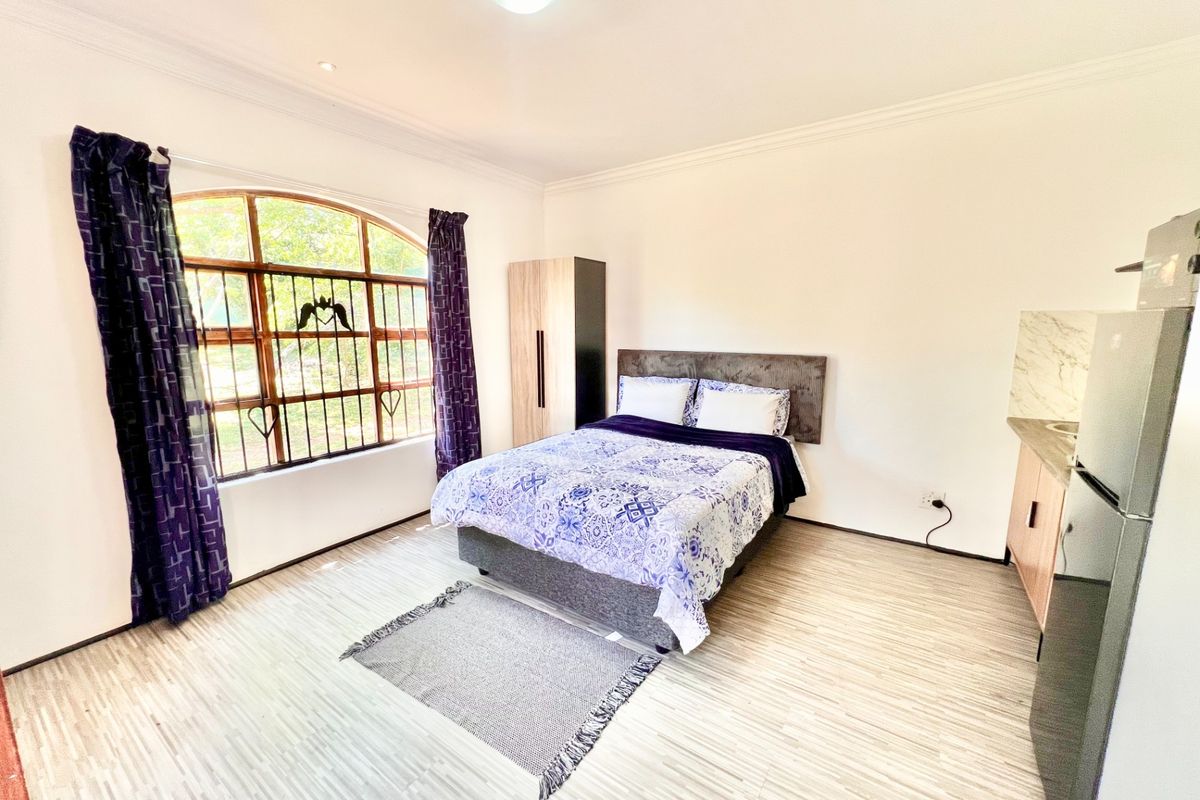 A well-lit bedroom featuring laminate flooring, an arched window with security bars, and built-in cabinetry.