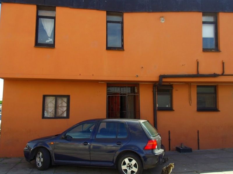 Front elevation of a two-story residential building featuring orange exterior walls, multiple windows, and a security gate entrance.