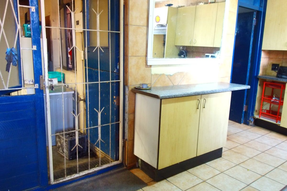 A functional kitchen area featuring built-in cabinetry, tiled flooring, and a security gate leading to an adjacent utility space.
