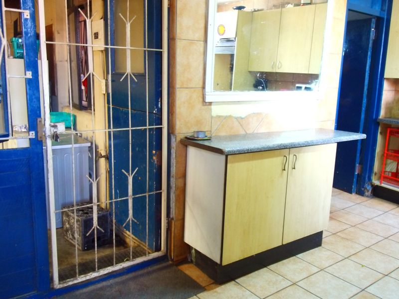 A functional kitchen area featuring built-in cabinetry, tiled flooring, and a security gate leading to an adjacent utility space.