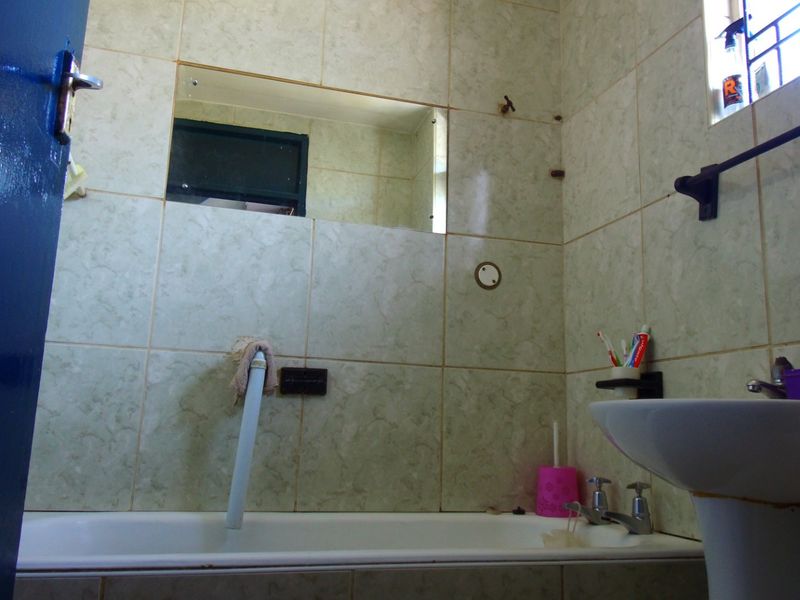 A dated bathroom featuring a bathtub, pedestal basin, and tiled walls, currently requiring maintenance and cosmetic updates to improve its functionality and aesthetic appeal.