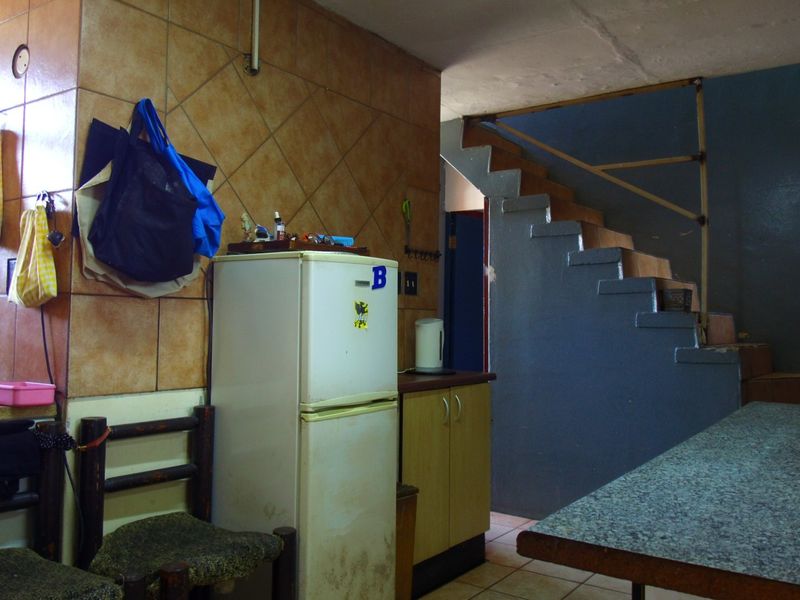 A dated kitchen area featuring tiled walls, built-in cabinetry, and an adjacent staircase, offering potential for modernization and renovation.