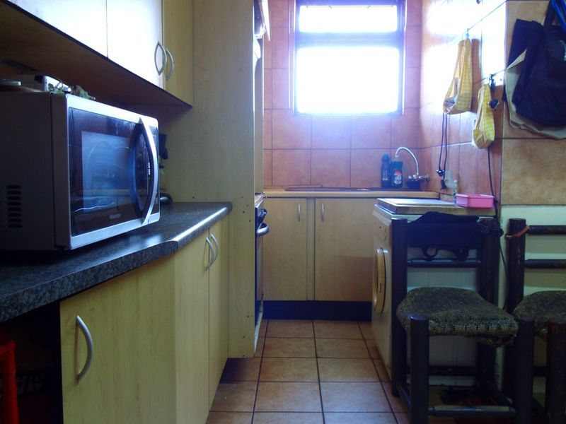 A compact kitchen featuring dated cabinetry, tiled walls and flooring, and integrated appliances, offering potential for a modern renovation.