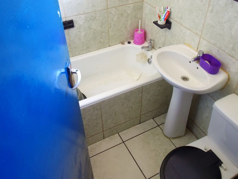 A compact bathroom featuring a standard bathtub, pedestal basin, and toilet with tiled finishes throughout.