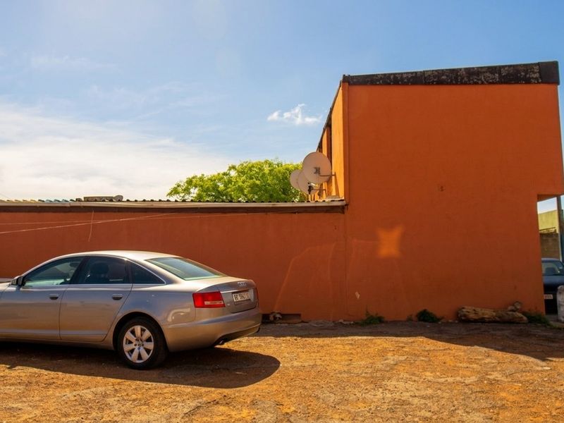 Rear exterior view of the property featuring a large orange facade, satellite dish, and an unpaved driveway area.