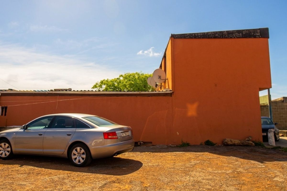 Rear exterior view of the property featuring a large orange facade, satellite dish, and an unpaved driveway area.