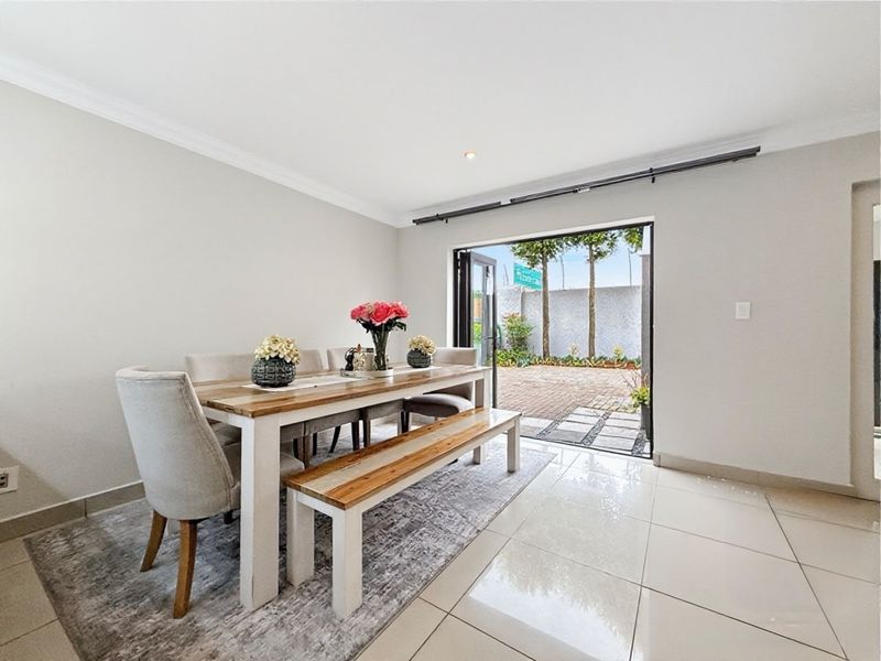 Bright dining area featuring large bi-fold doors that open onto a paved patio, complemented by neutral walls and polished floor tiles.