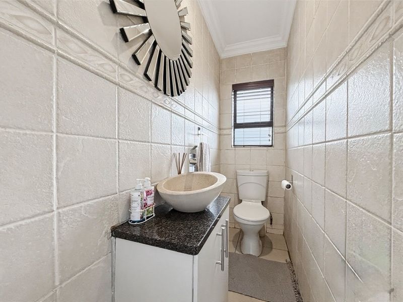 A compact guest bathroom featuring full-height wall tiling, a modern vessel sink on a granite-topped vanity, and a standard toilet.