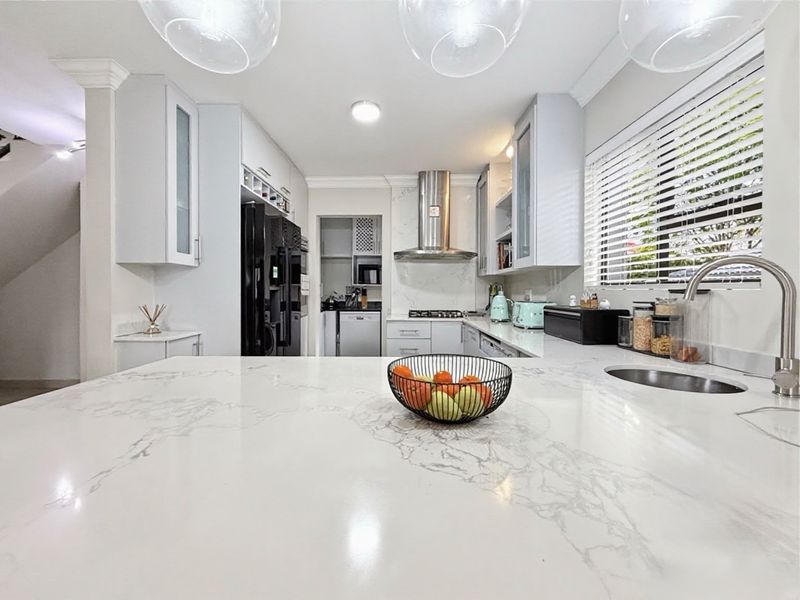 Modern kitchen featuring marble-look stone countertops, stainless steel extractor fan, gas hob, and a convenient adjoining scullery area with ample cabinetry.