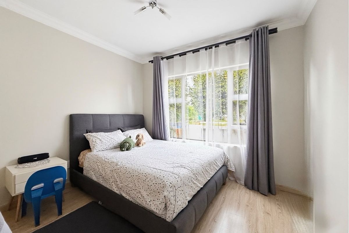 A well-maintained bedroom featuring light-toned laminate flooring, neutral wall finishes, and a large window with installed curtain rods.