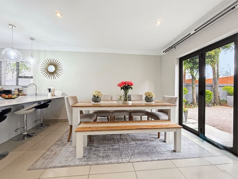 Bright open-plan dining and kitchen area featuring a breakfast island, modern tiled flooring, and large glass doors opening to the rear patio.