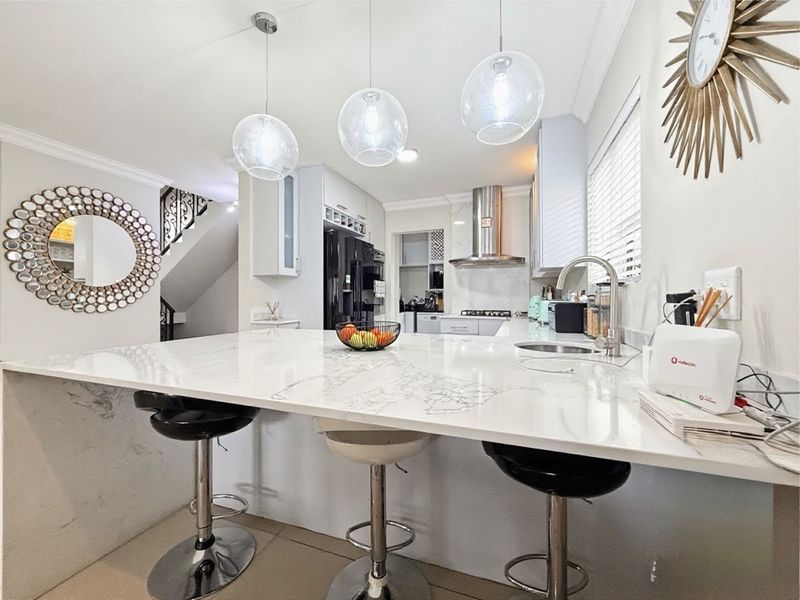 Modern kitchen featuring a large marble-look stone island with breakfast bar seating, sleek cabinetry, stainless steel extractor fan, and elegant pendant lighting.