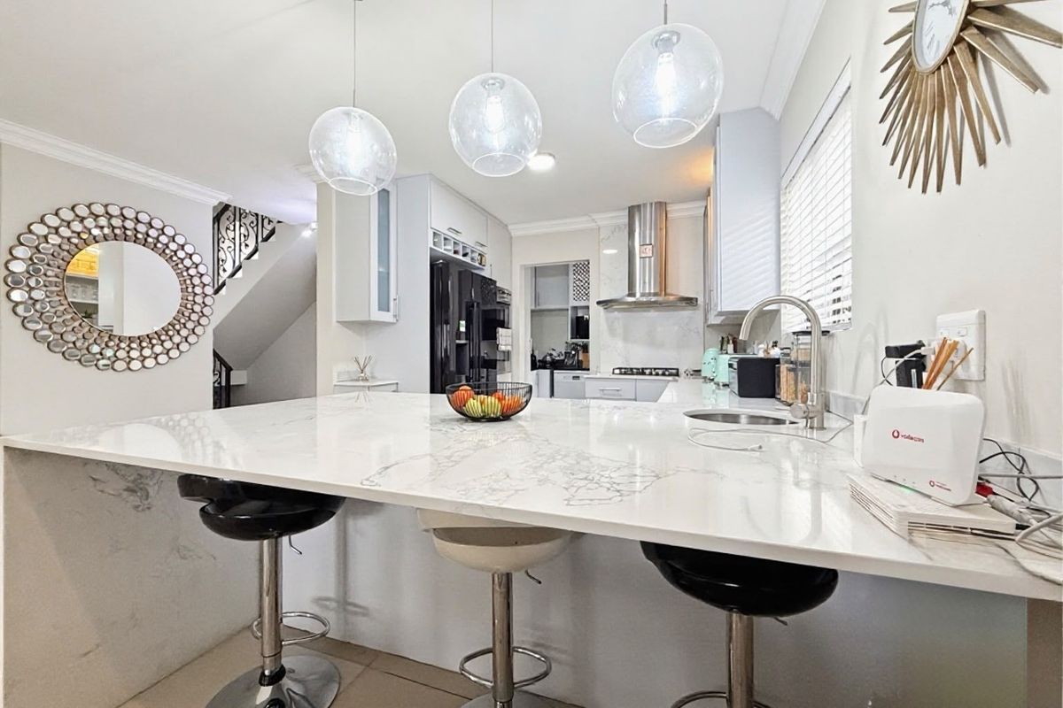 Modern kitchen featuring a large marble-look stone island with breakfast bar seating, sleek cabinetry, stainless steel extractor fan, and elegant pendant lighting.