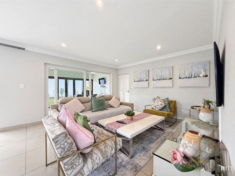 A bright and spacious living room featuring neutral tiled flooring, recessed downlighting, and large sliding glass doors providing access to the outdoor area.