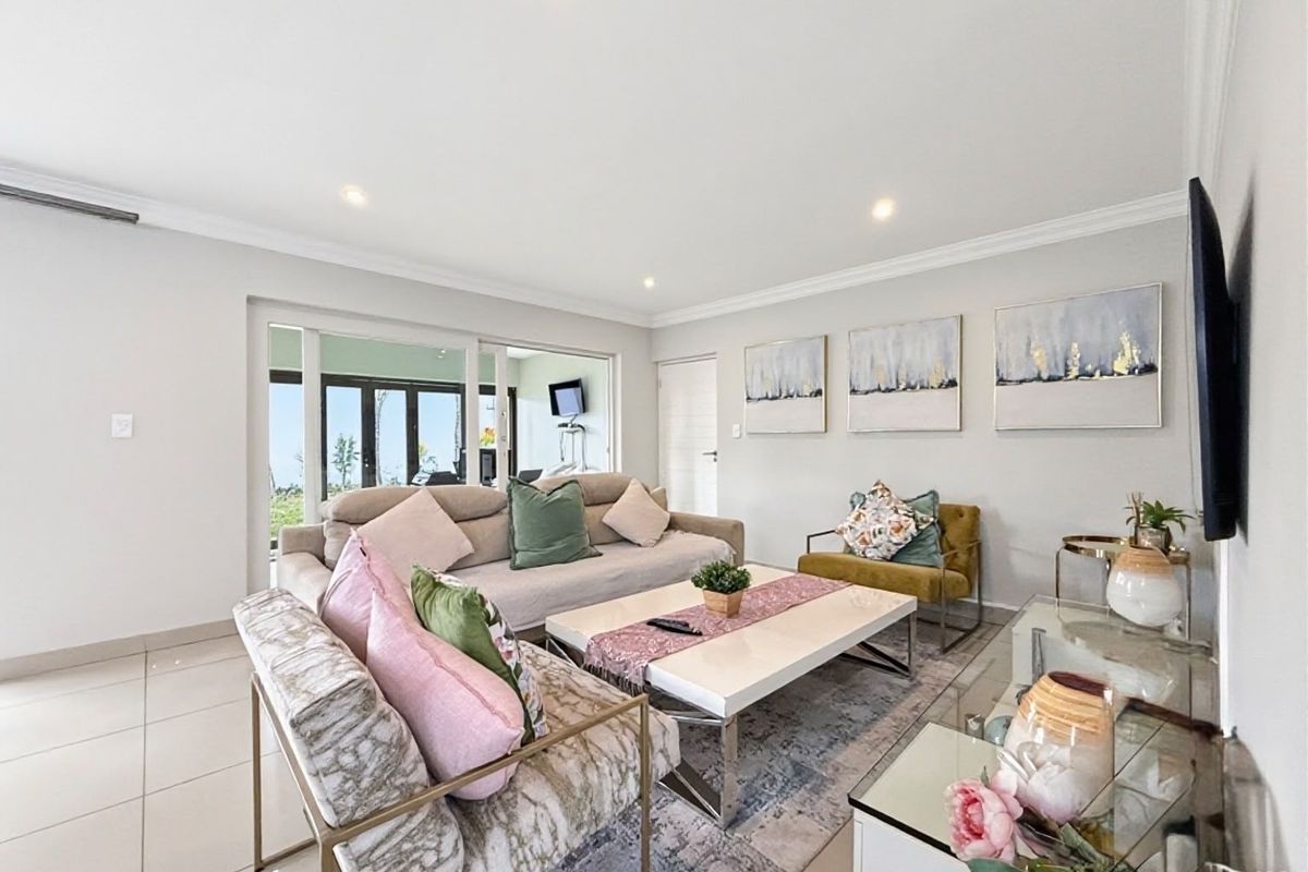 A bright and spacious living room featuring neutral tiled flooring, recessed downlighting, and large sliding glass doors providing access to the outdoor area.
