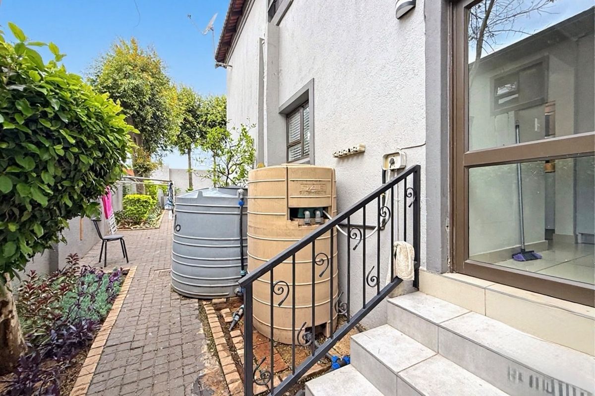 Rear exterior view featuring a paved walkway, tiled steps with a wrought iron handrail, and two water storage tanks against the building wall.