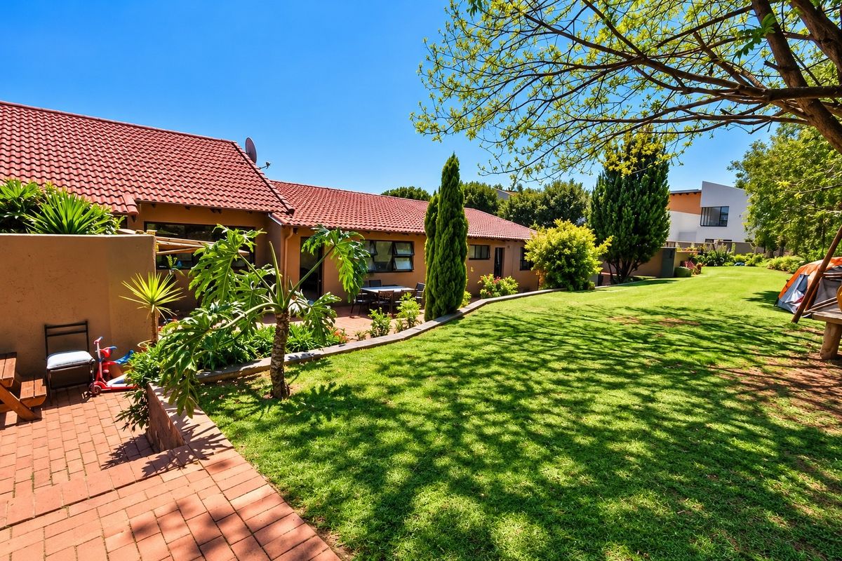 A spacious rear garden featuring a brick-paved patio area, well-maintained lawn, and a classic terracotta tiled roof structure.