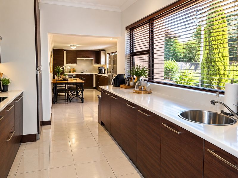 Modern kitchen featuring dark wood cabinetry, white stone countertops, stainless steel sink, and integrated appliances, with a view into the adjacent dining area.