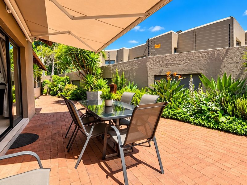 A well-maintained outdoor patio featuring brick paving, a retractable awning, and direct access to the home through large sliding glass doors.