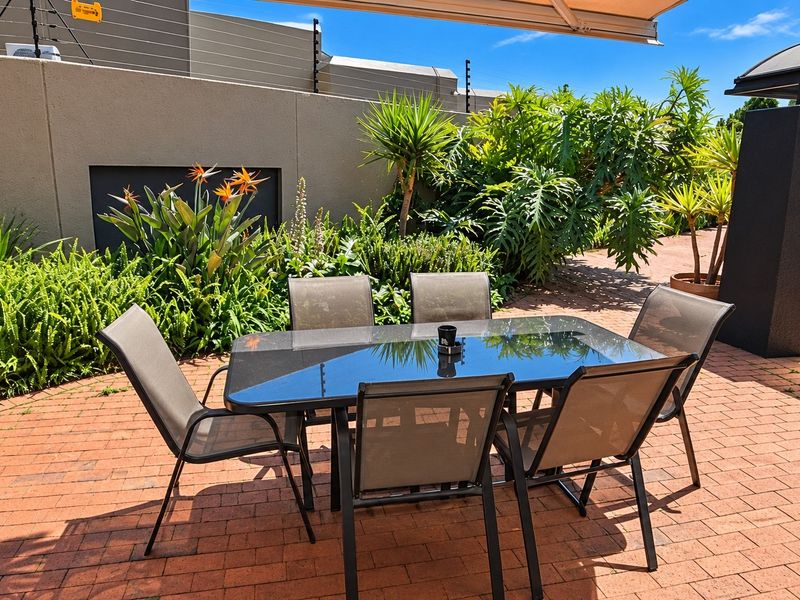 A well-maintained outdoor patio area featuring brick paving, a retractable awning, and a secure perimeter wall with electric fencing.