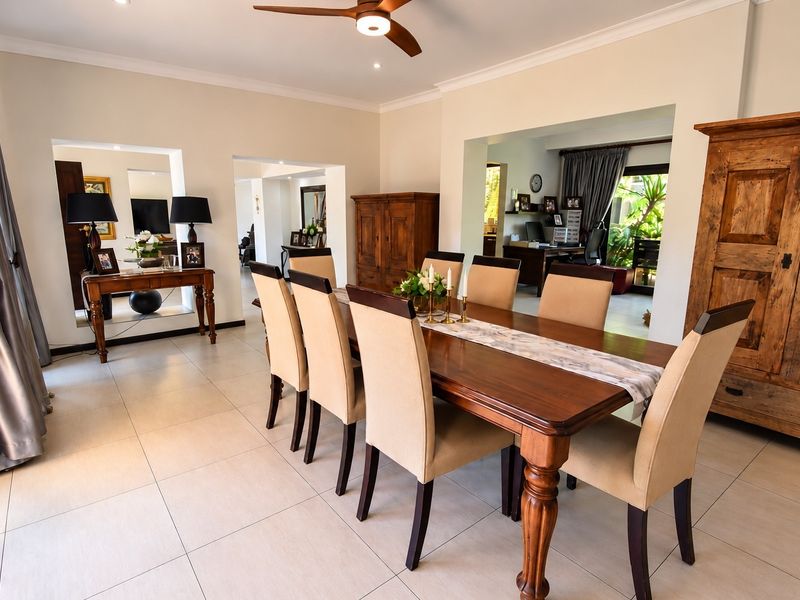 Spacious dining room featuring neutral tiled flooring, coved cornicing, and a ceiling fan, with open-plan access to adjacent living and study areas.