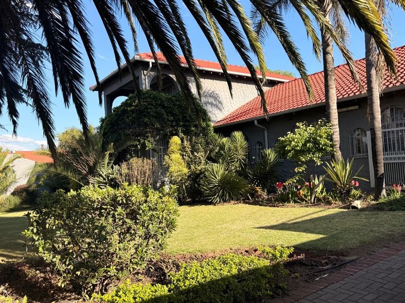 A well-maintained rear garden featuring a lush lawn, mature palm trees, and a house exterior with terracotta roof tiles and grey rendered walls.