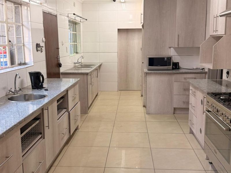 A well-maintained kitchen featuring light wood cabinetry, granite countertops, tiled finishes, and a gas stove with an integrated extractor fan.