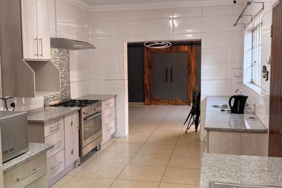 Spacious kitchen featuring granite countertops, built-in cabinetry, gas stove with extractor, and tiled finishes throughout, leading into an adjacent living area.