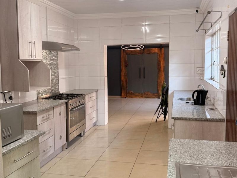 Spacious kitchen featuring granite countertops, built-in cabinetry, gas stove with extractor, and tiled finishes throughout, leading into an adjacent living area.