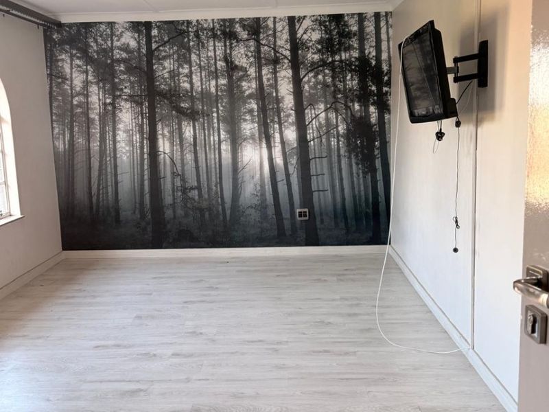 An empty bedroom featuring light-toned laminate flooring, recessed ceiling lighting, and a feature wall with a forest mural.