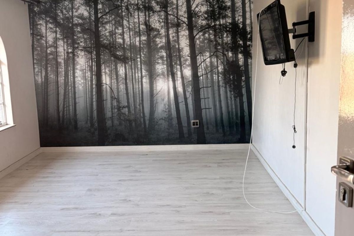 An empty bedroom featuring light-toned laminate flooring, recessed ceiling lighting, and a feature wall with a forest mural.
